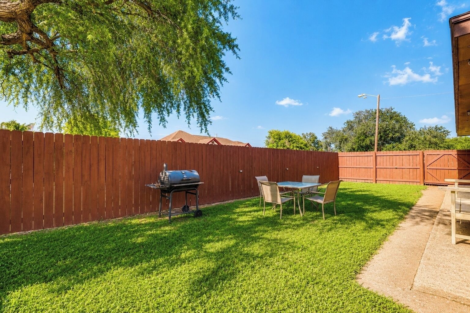 A backyard with a wooden fence, a grill, and a table with chairs.