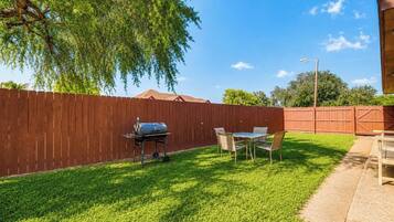 A backyard with a wooden fence, a grill, and a table with chairs.
