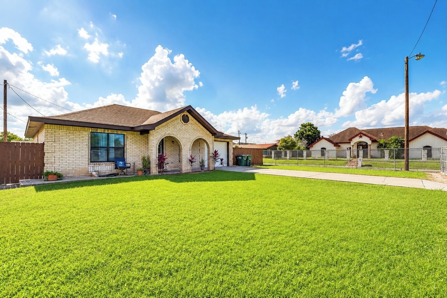 A residential property with a well-maintained lawn, a brick house with a porch, and a clear sky.