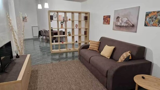 A modern living room with a brown sofa, a wooden coffee table, and a glass partition. There are paintings on the wall and a fireplace. - DONNA RUDIAE WILL HOST YOU IN THE HEART OF SALENTO, IN THE CENTER OF DELICIOUS LECCE. (Lecce)