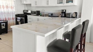 Una cocina moderna con armarios blancos, una isla central con taburetes de bar, estufa, microondas y varios electrodomésticos.