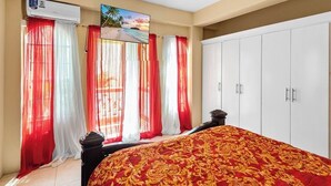 Un dormitorio con cama, armario y ventana con cortinas rojas y blancas.