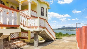 Un edificio con una escalera que lleva a un balcón, vista hacia un cuerpo de agua y una montaña al fondo.