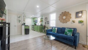 A spacious living area with a blue sofa, a glass coffee table, and a kitchen in the background. - Private Deck • Pet Friendly • Spacious Courtyard (St. Petersburg)