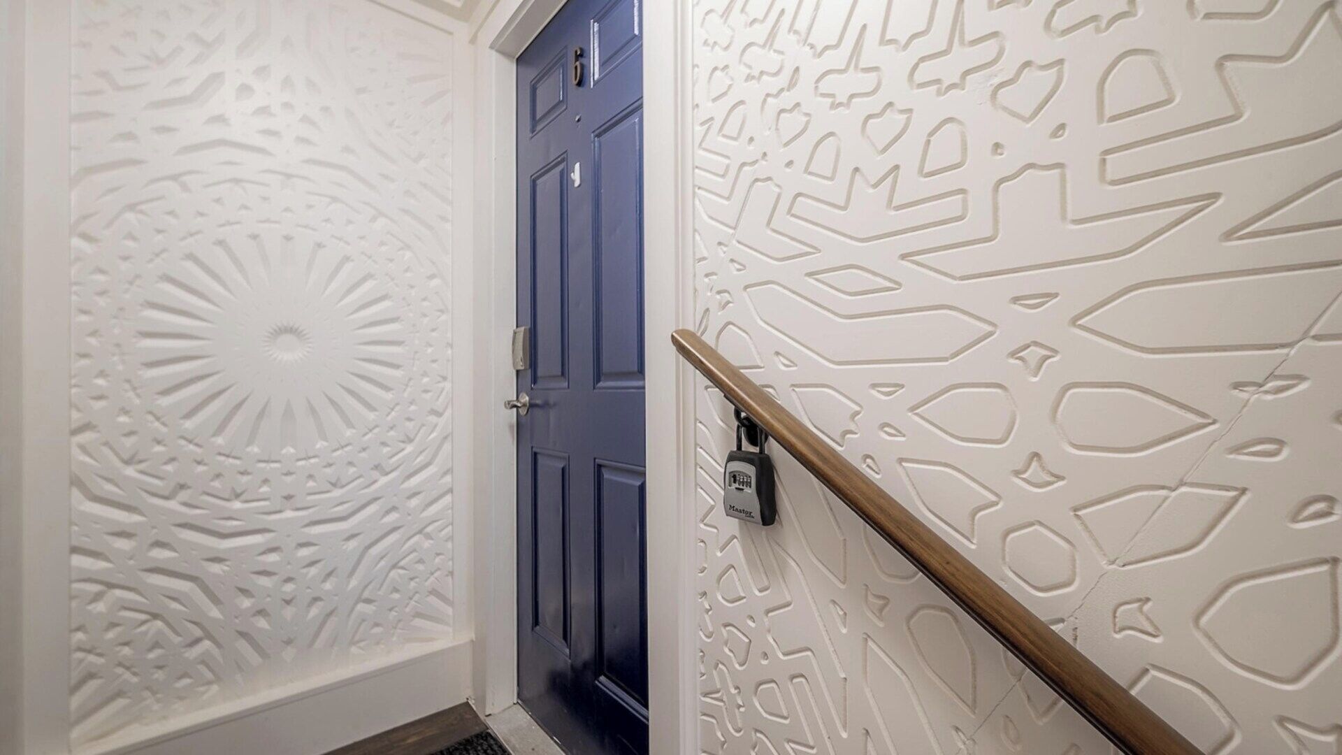A hallway with a blue door, decorative white wall panels, and a handrail.