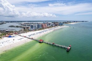 An aerial view of a coastal city with a long pier extending into the water, a beach with sun loungers, and a marina with boats. - Private Deck • Pet Friendly • Spacious Courtyard (St. Petersburg)