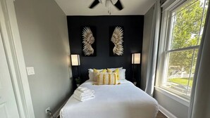 A bedroom with a bed, two wall-mounted lamps, a ceiling fan, and a window with curtains. - Near Lake and Museum • Modern • Game Area (Chicago)