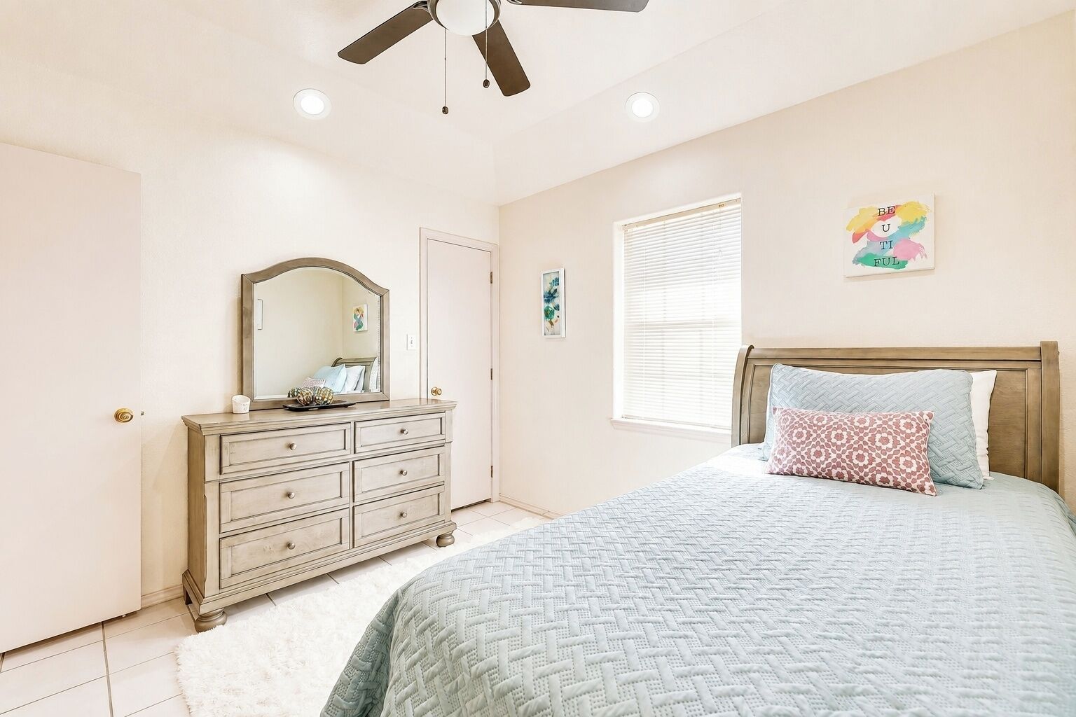 A bedroom with a bed, dresser, ceiling fan, and a window with blinds.