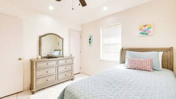 A bedroom with a bed, dresser, ceiling fan, and a window with blinds.