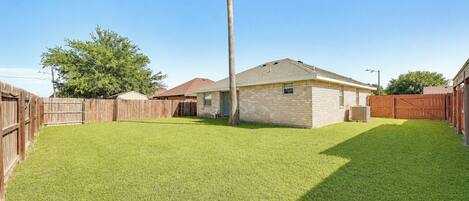 A backyard with a wooden fence, a single-story house, and a palm tree.