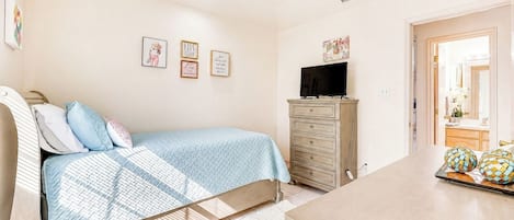 Un dormitorio con cama, cómoda, televisor y una obra de arte en la pared.