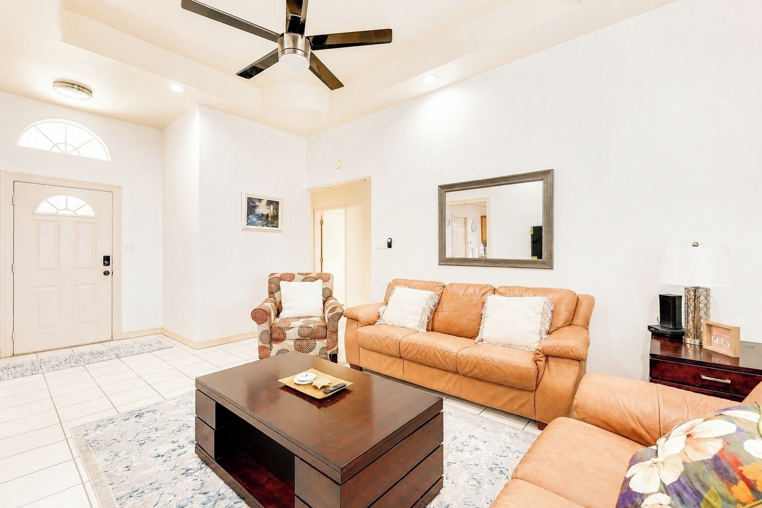 A living room with a sofa, armchair, coffee table, and a ceiling fan.