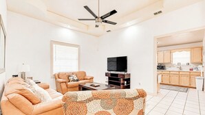 Uma sala de estar com sofá, mesa de centro, televisão e ventilador de teto.