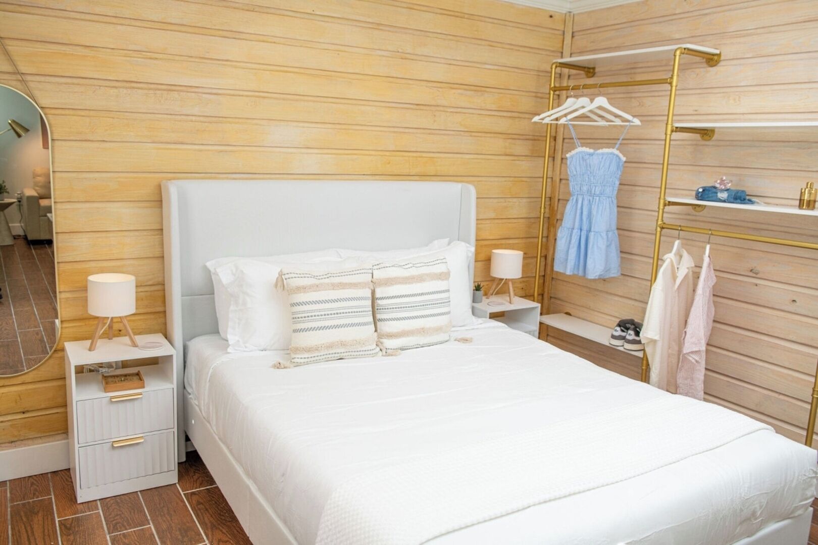 Ein ordentlich eingerichtetes Schlafzimmer mit einem großen Bett, Nachttischen, einem Kleiderständer und einem Spiegel.