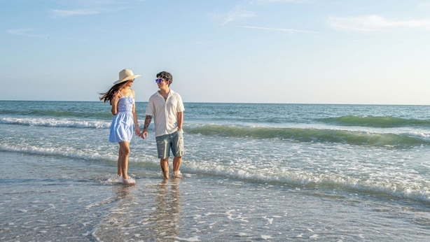 Un couple se promène sur une plage, avec des vagues en arrière-plan.
