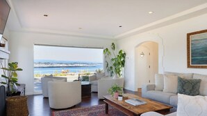 Un salon spacieux doté d’une grande fenêtre donnant sur le bord de l’eau, et aménagé avec un canapé, des fauteuils et une table basse.