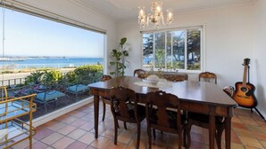 Un espace repas avec vue sur la mer, un lustre et une guitare.