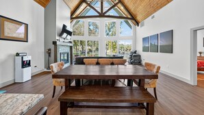 Un comedor espacioso con una gran mesa de madera y sillas acolchadas, una cocina integrada y ventanas amplias que ofrecen vistas al exterior.