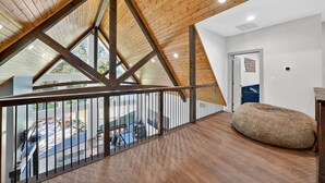 Un loft espacioso con techo alto, vigas de madera, un gran sillón informal y vista al patio trasero.