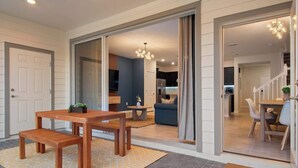Un interior moderno con una mesa de comedor de madera, un sofá y una zona de cocina visible a través de una puerta abierta.