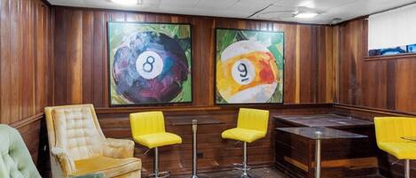 A bar area with wooden paneling, a green upholstered chair, and yellow bar stools.