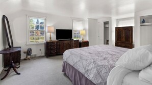 Quarto com uma cama grande, duas mesas de cabeceira com luminárias, cômoda, televisão e espelho.