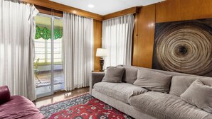 Sala de estar com um sofá cinza, um tapete vermelho estampado e uma parede de madeira com um desenho circular.