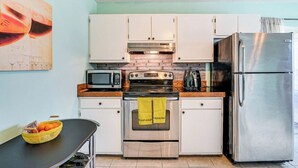 Eine kompakte Küche mit weißen Schränken, einem Edelstahl-Kühlschrank, einer Mikrowelle, einem Backofen und einer Kaffeemaschine.