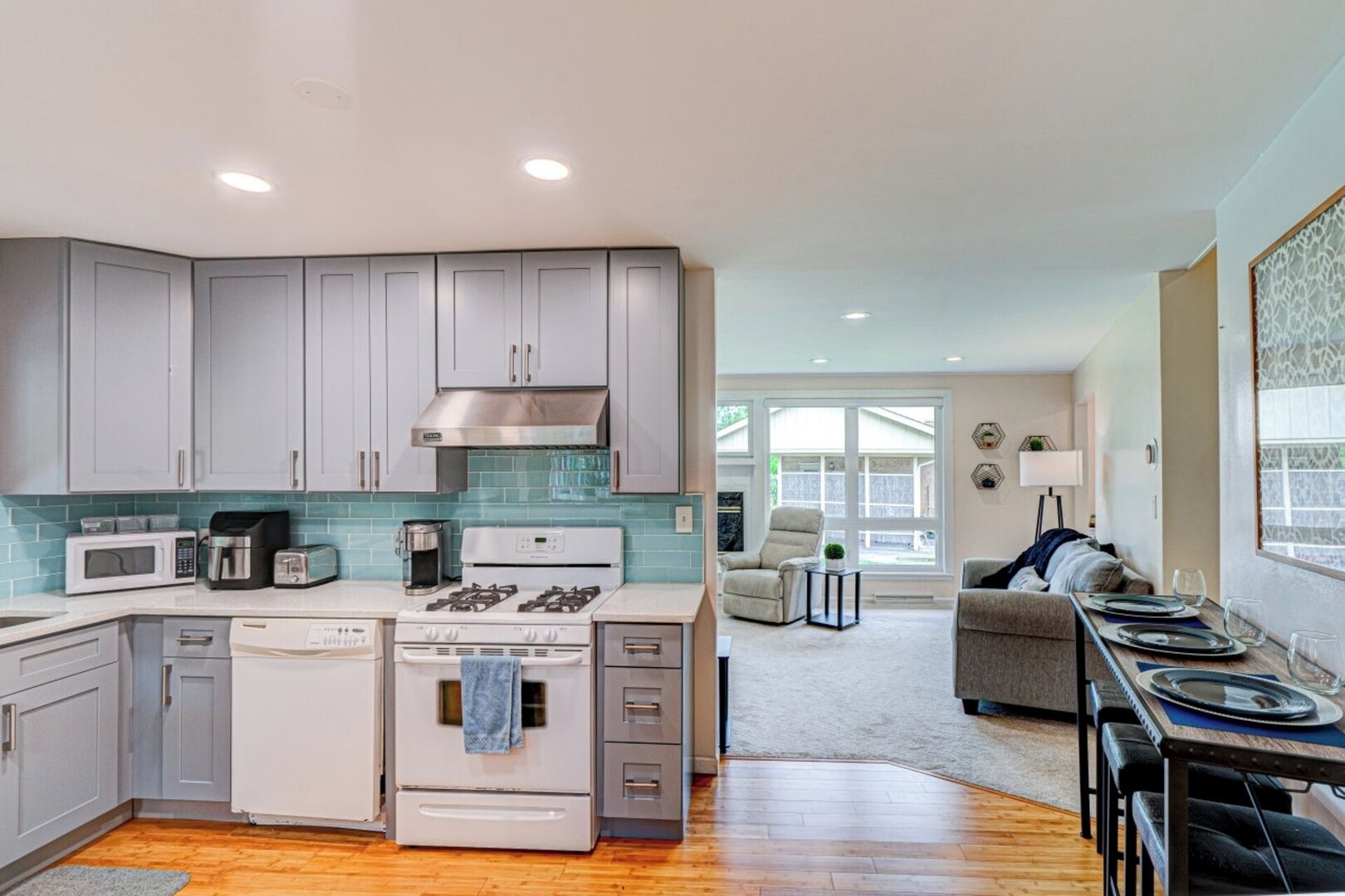 A modern kitchen with grey cabinets, a white dishwasher, a stove, and a coffee maker.