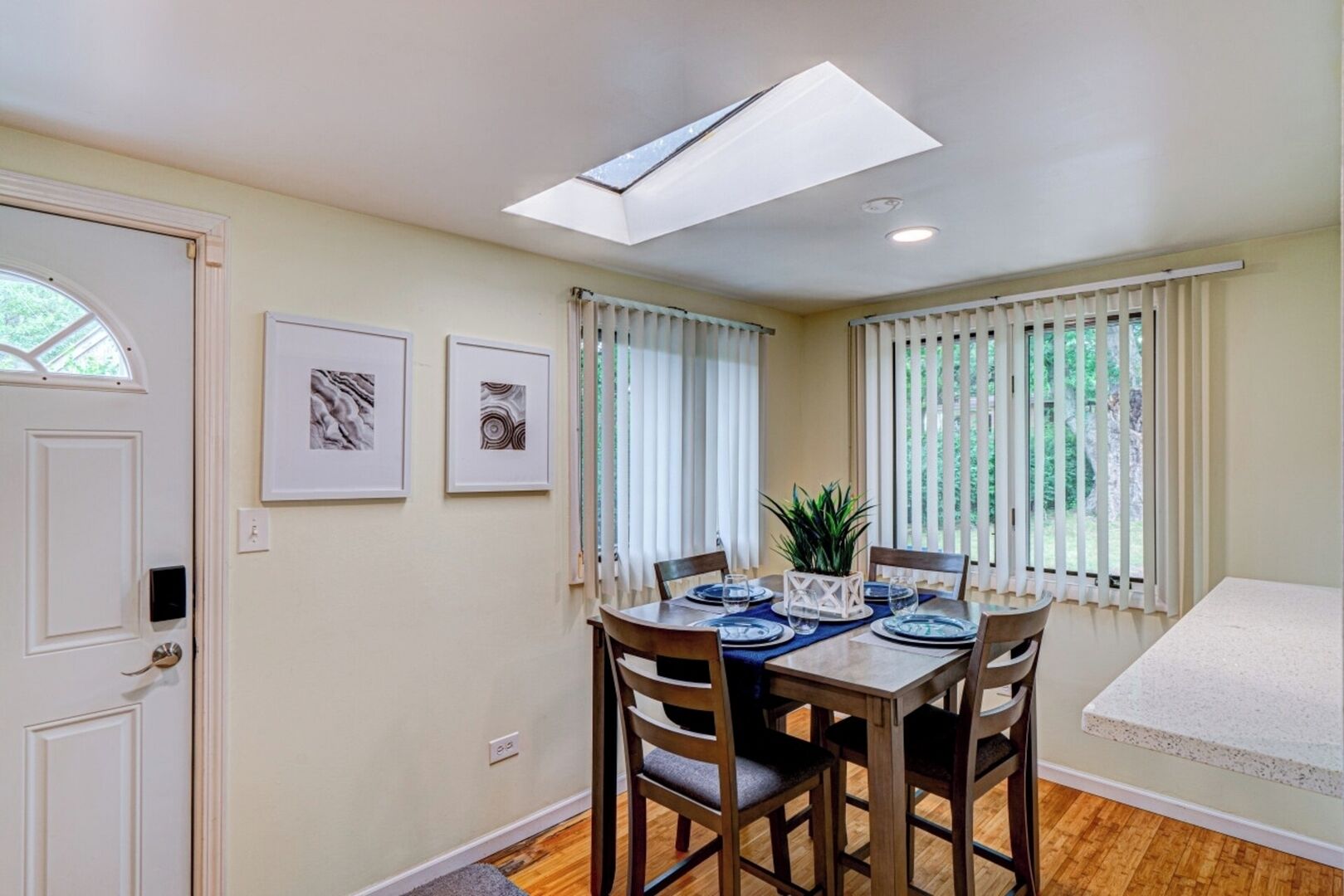A dining area with a table set for four, a ceiling light, and a window with blinds.