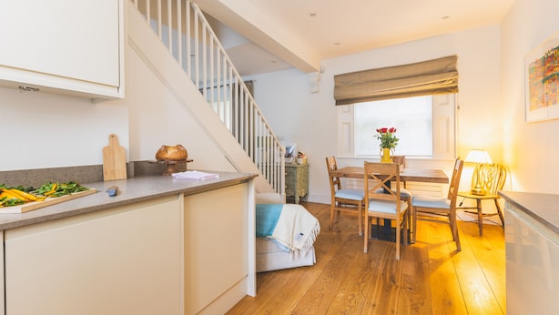 Een keuken met een houten aanrecht, een eethoek met tafel en stoelen, een trap en een raam met uitzicht.