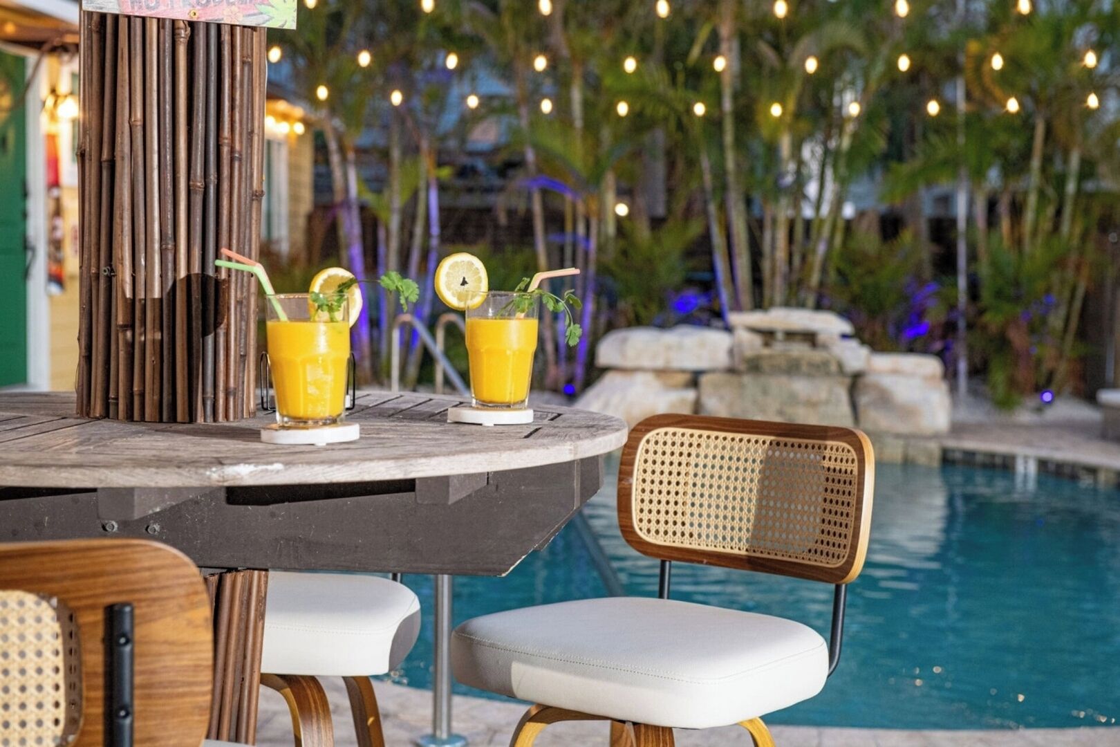 Un bar junto a la piscina con dos vasos de zumo de naranja, una silla de madera y una de mimbre.