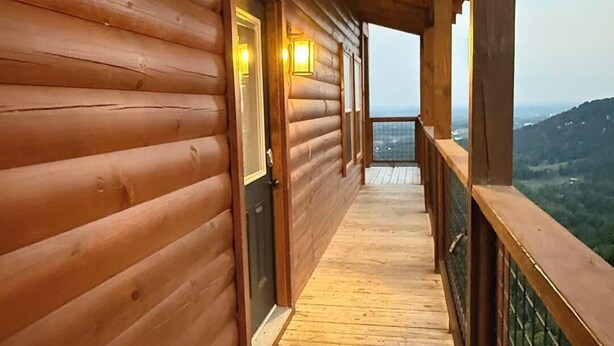 Eine Holzhütte mit einer überdachten Holzterrasse, die zu einer Tür mit zwei Lampen führt.