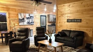 Ein gemütliches Cabin-Interieur mit Essbereich, zwei Ledersesseln, einem Couchtisch, einer Couch und einer Küche im Hintergrund.