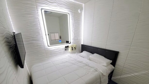 Un dormitorio moderno con una cama grande, un espejo montado en la pared y una mesita de noche con lámpara.