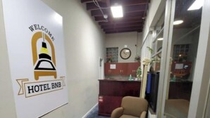 Un pasillo de hotel con una recepción, un reloj y un letrero que dice "WELCOME HOTEL BNB".