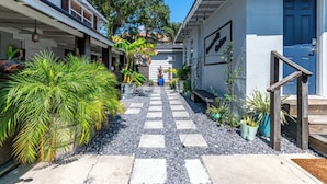 A narrow pathway leading to a building with a blue door, surrounded by potted plants and a small bench. - Spacious Courtyard • Private Deck • Pet Friendly (St. Petersburg)