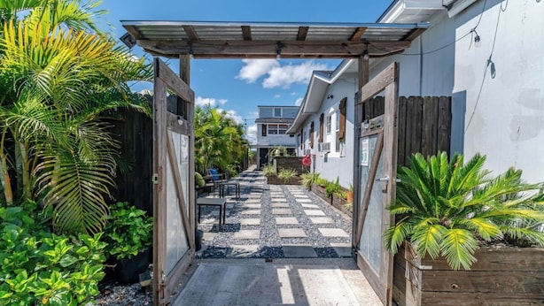 A narrow pathway leading to a building with a covered entrance, surrounded by lush greenery and potted plants. - Spacious Courtyard • Private Deck • Pet Friendly (St. Petersburg)