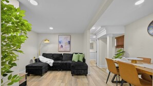 A modern living room with a sectional sofa, a dining table with chairs, and a large plant. - Spacious Courtyard • Private Deck • Pet Friendly (St. Petersburg)