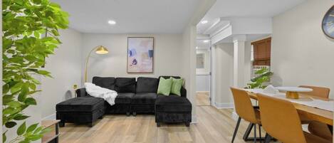 A modern living room with a sectional sofa, a dining table with chairs, and a large plant.