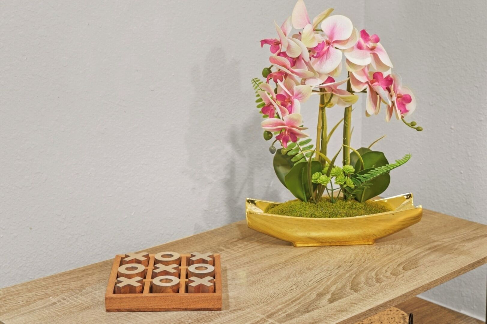 A wooden table with a small potted orchid plant and a wooden tic-tac-toe game.