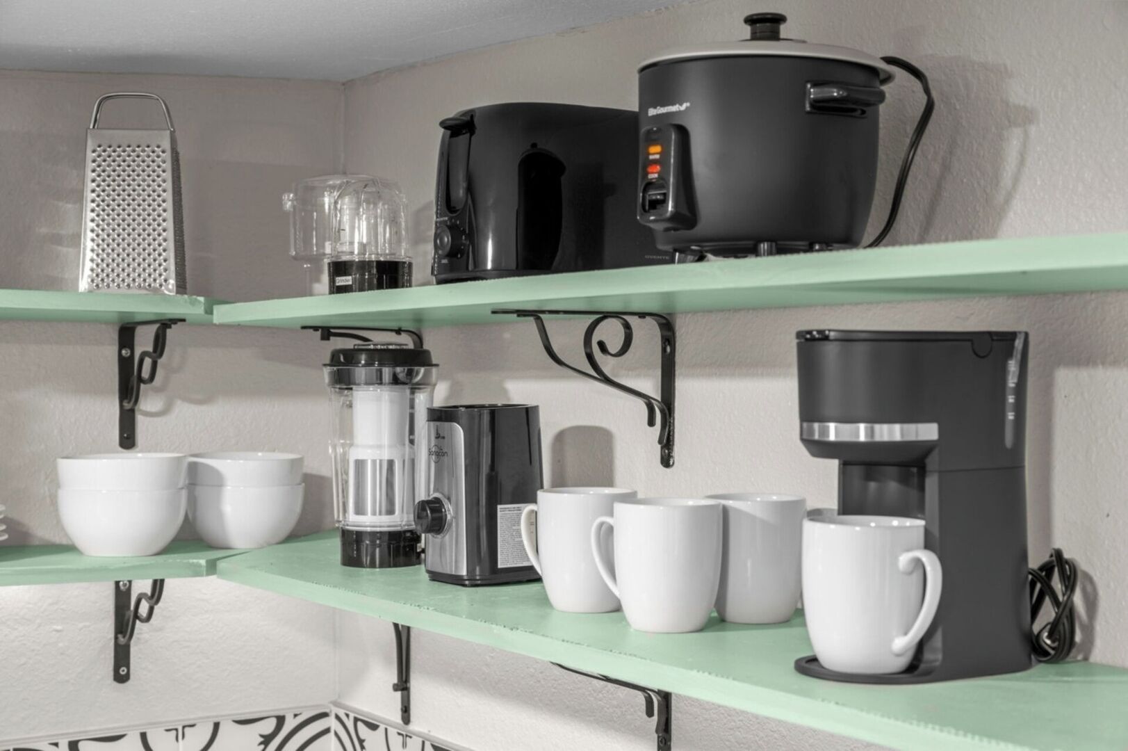 Een keuken met planken waarop diverse apparaten staan, zoals een koffiezetapparaat, een blender en een rasp.