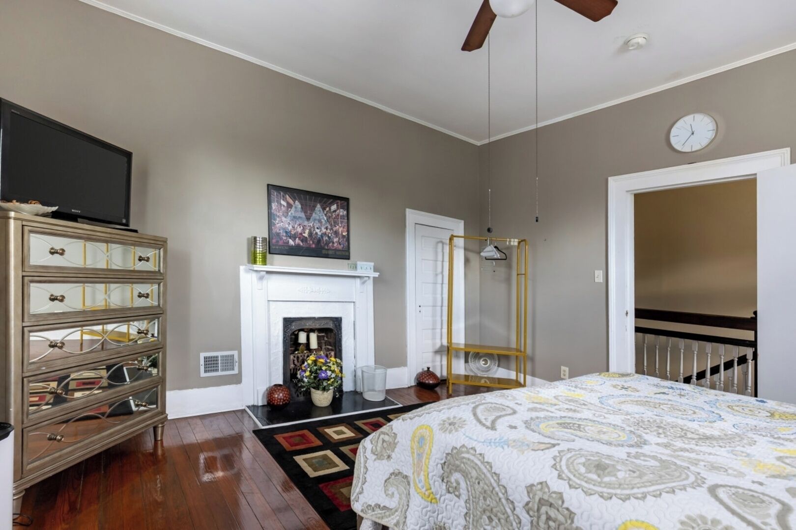 Une chambre avec une cheminée, un lit recouvert d’une couvre-lit à motifs, une commode avec des miroirs et un téléviseur posé sur le dessus.