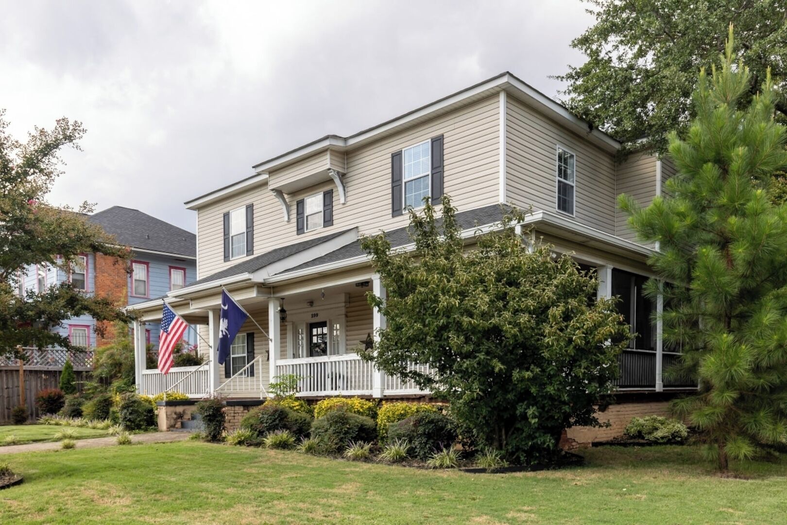 A two-story house with a front porch, a flag, and a well-maintained lawn.