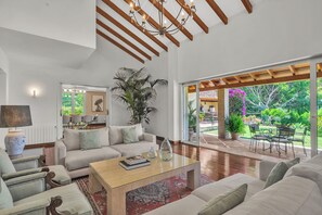 A spacious living room with a large window, a chandelier, and a dining area with outdoor seating. - Villa El Paular – Great Location (Marbella)