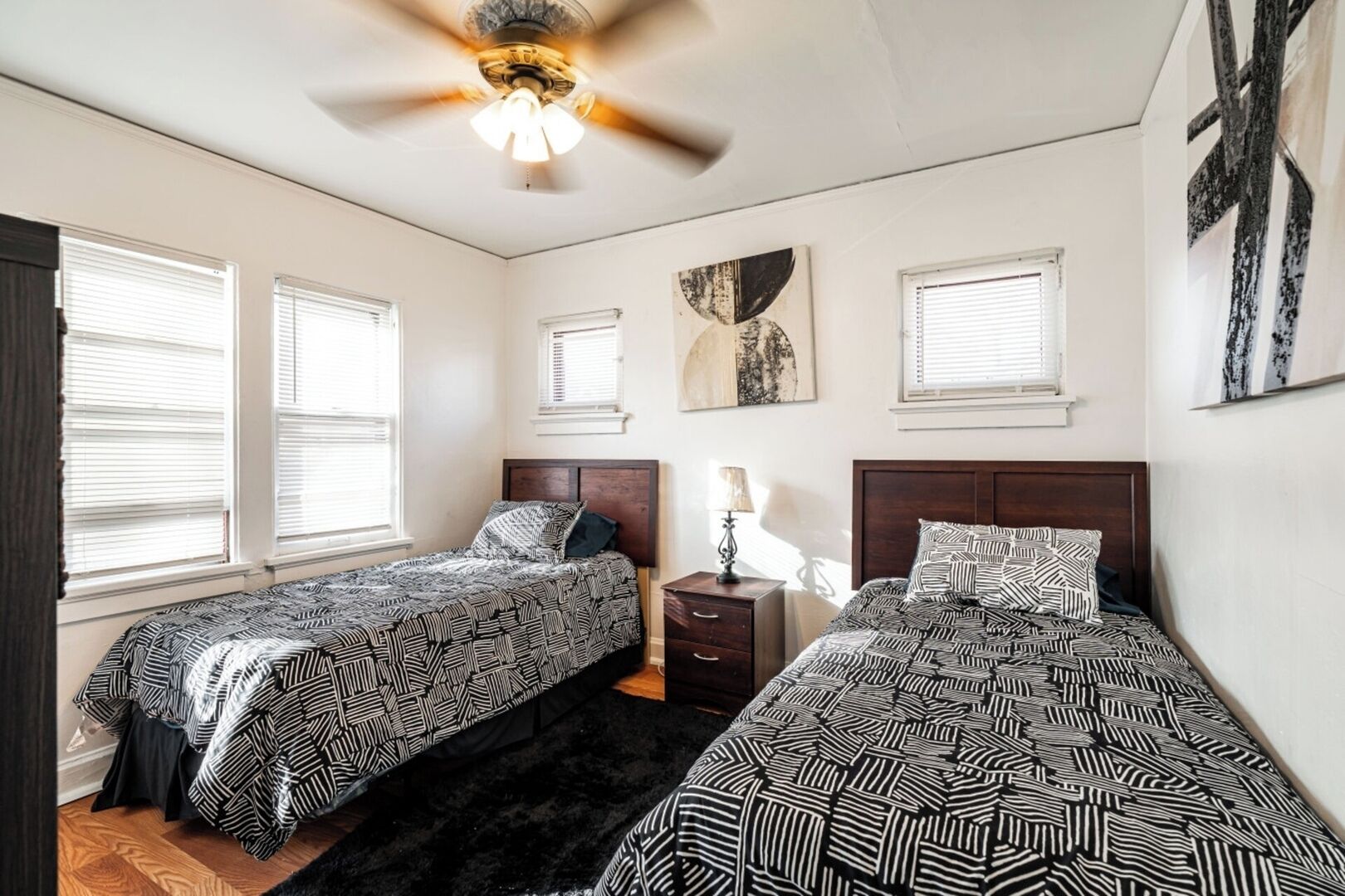 A bedroom with two beds, a ceiling fan, and artwork on the walls.