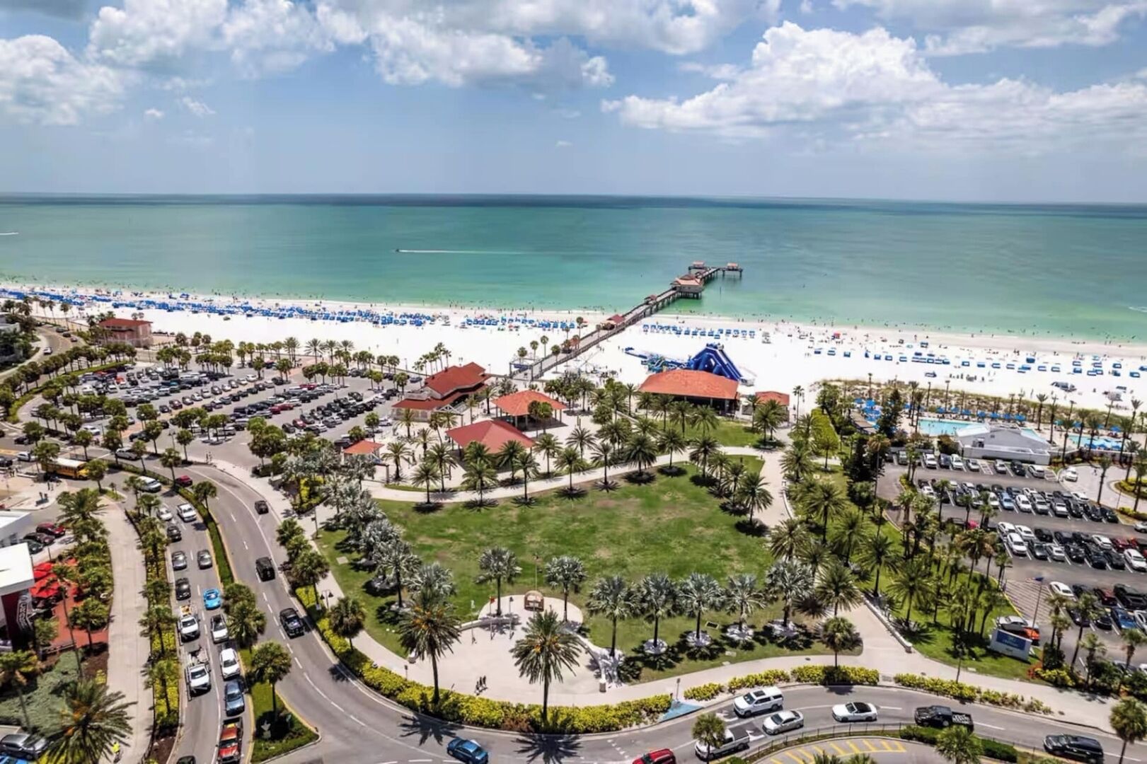 Vista aerea di una località balneare con spiaggia, parcheggi e un molo che si estende nell'oceano.