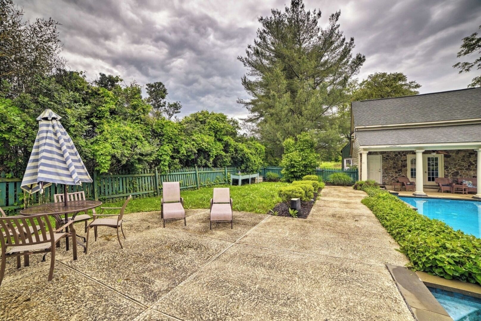 A backyard with a pool, lounge chairs, and a covered patio area.