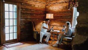 Interior rústic d'una cabana de fusta amb una porta de fusta, una làmpada, una taula rodona petita i dues persones assegudes en un sofà.