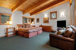 Een ruime slaapkamer met een groot bed, een bruine leren bank, houten balken in het plafond en een televisie.